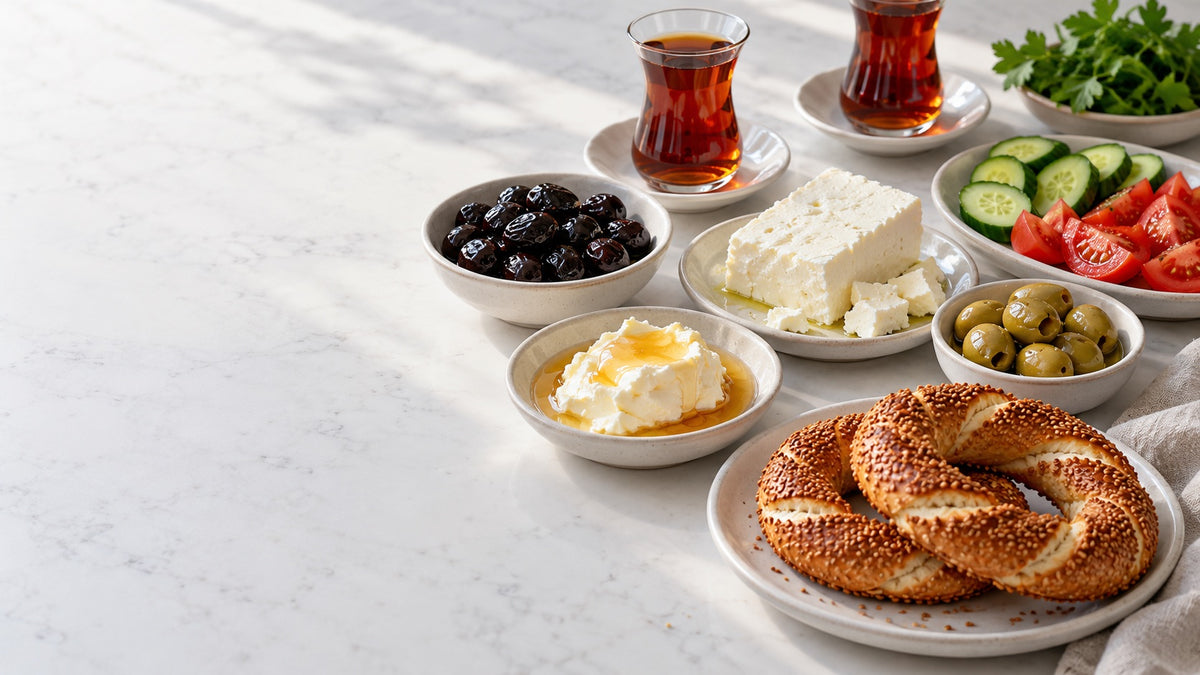 Turkish breakfast on a white counter: white cheese, black and green olives, clotted cream with honey, simit and two glasses of tea